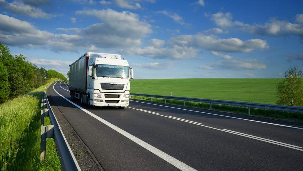 Vit lastbil på vägen i ett sommarlandskap använder Nestes motoroljor och smörjmedel